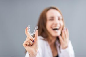 beautiful smiling turkish woman is holding an invisalign bracer in a studio with grey background