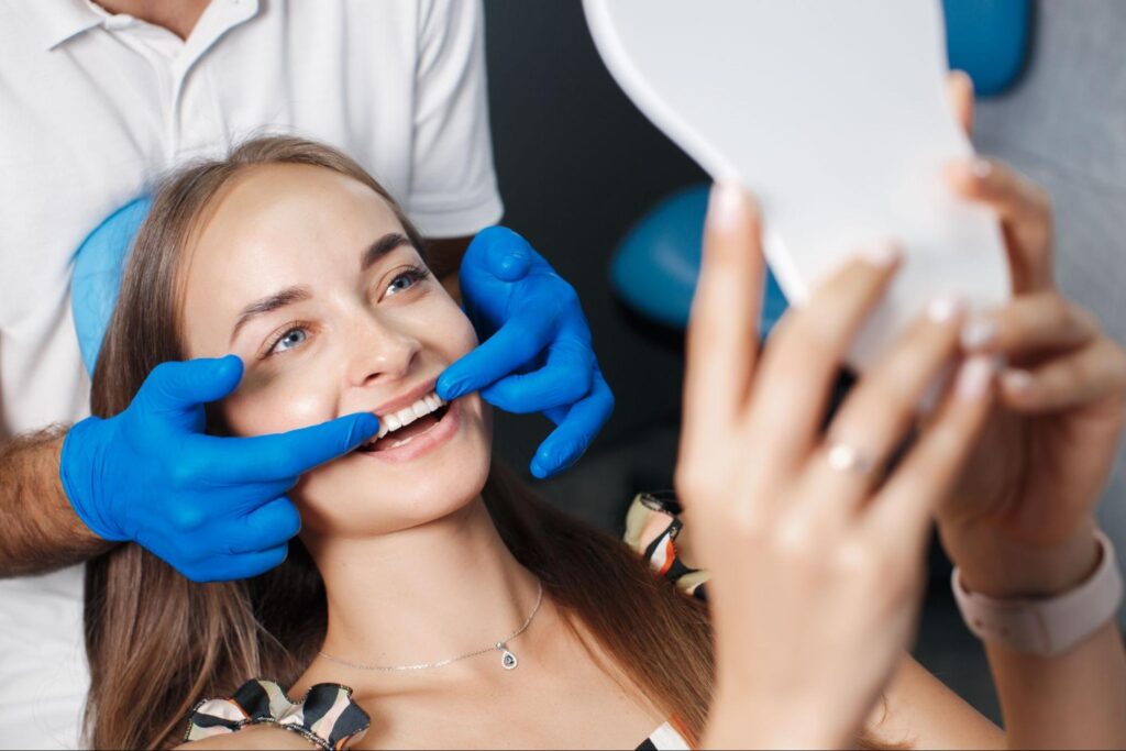 woman smiling and looking at mirror with dentist behind